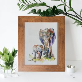Elephant and calf watercolour painting framed in mid-brown wooden photo frame on a table