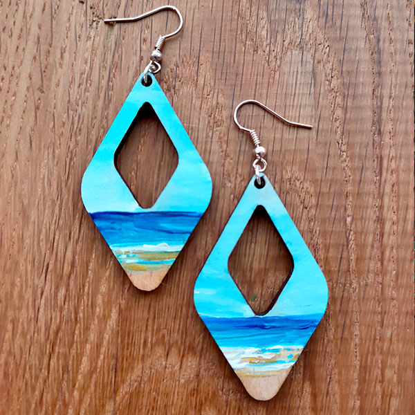 Hand painted wooden earrings featuring a beach and deep blue sea.