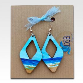 Hand painted wooden earrings featuring a beach and deep blue sea on rustic card with blue bow.